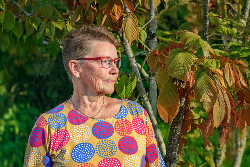 Vanhempi nainen värikkäässä paidassa katsoo puistossa sivulle.