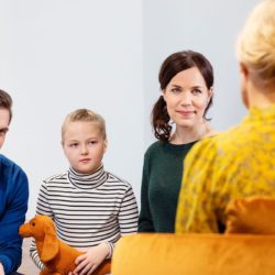 Perhe keskustelee keltapaitaisen naisen kanssa.
