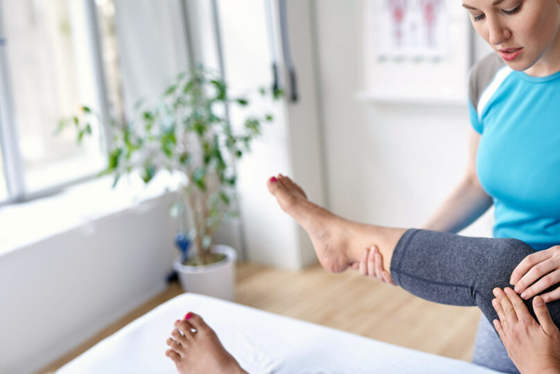 Fysioterapeutti pitää naisasiakkaan jalkaa koholla