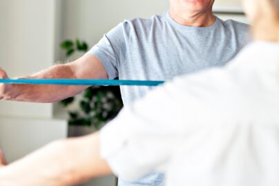 naisterapeutti ohjaa miesasiakasta tekemaan liikkeita jumppakuminauhalla