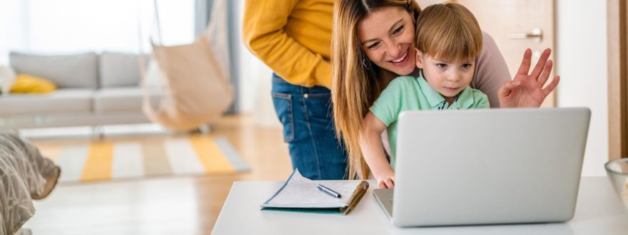 nainen ja poikalapsi tietokoneella kotona taustalla muu perhe