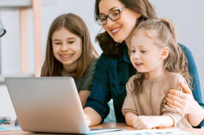 nainen ja kaksi lasta tietokoneella hymyilemassa