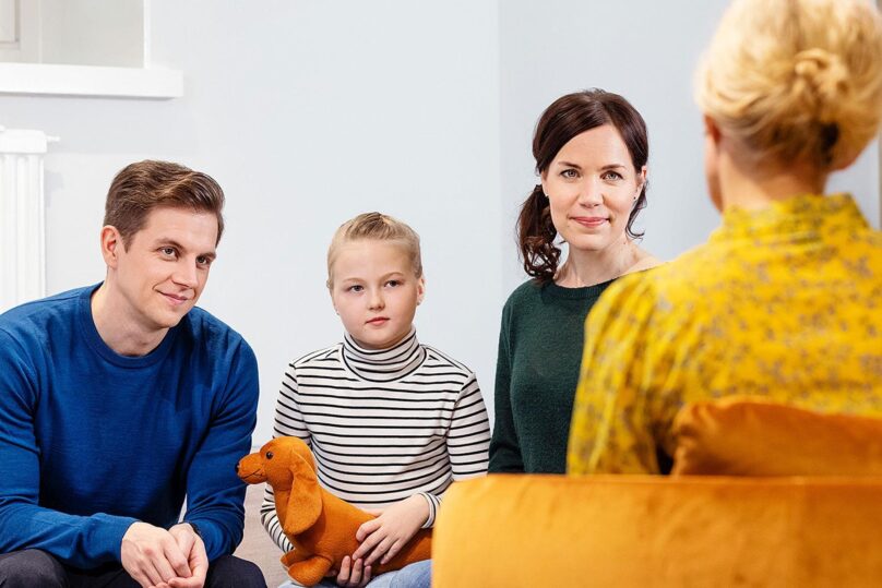 Perhe keskustelee keltapaitaisen naisen kanssa.