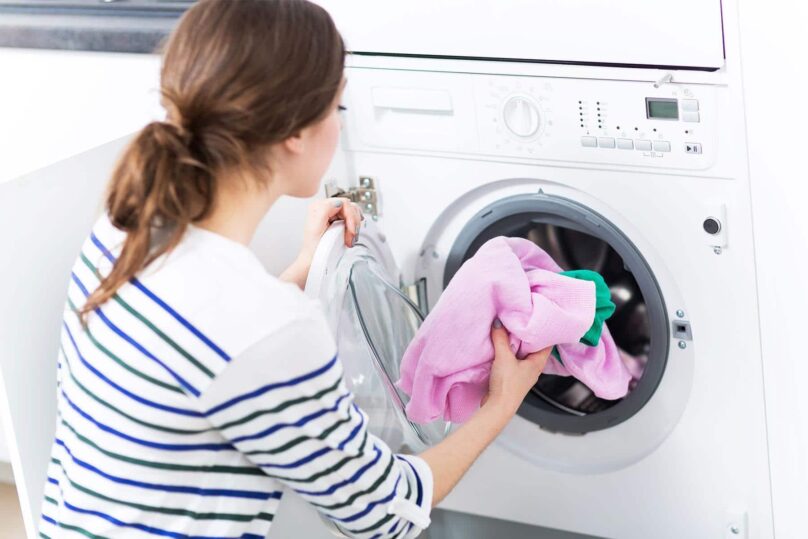 nainen_tayttaa_pyykinpesukonetta_vaatteilla