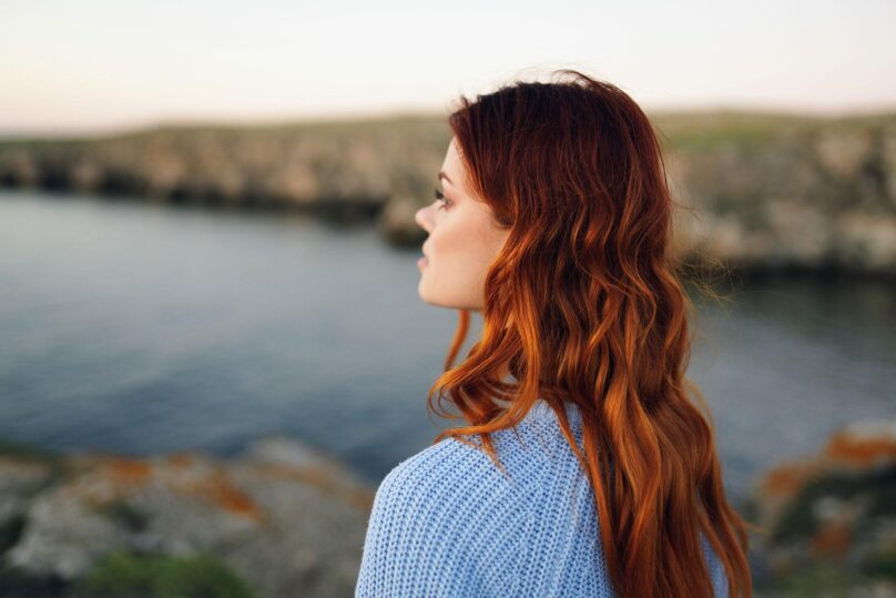 nuori punahiuksinen nainen katsoo horisonttiin ulkona veden aarella