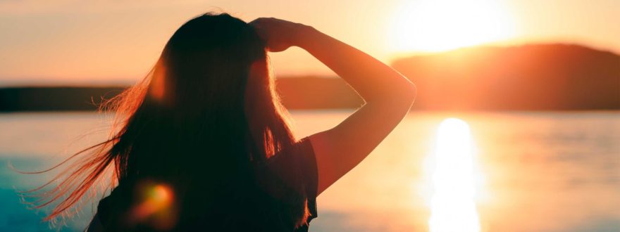 Nainen katsoo auringonlaskua merellä.