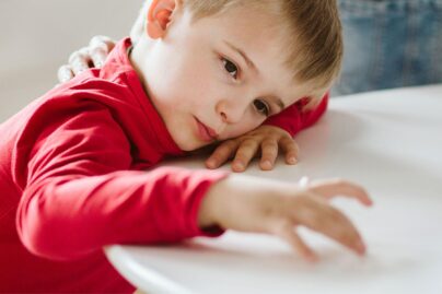 poika nojaa kateen ja poytaan ja nayttaa kyllastyneelta