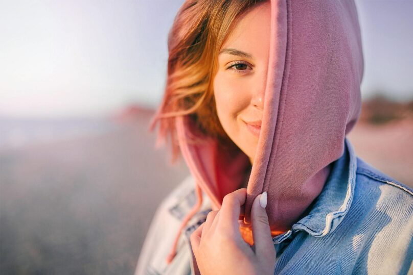 Nuori nainen rannalla huppu paassa hymyilee