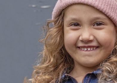 lapsi hymyilee kameraan ja pitää pensseliä kädessään
