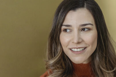 Keski-ikäinen nainen katsoo sivuun oranssineule päällään.