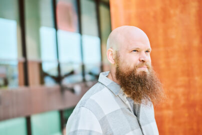 Mies, jolla parta, seisoo oranssiseinäisen talon edessä.