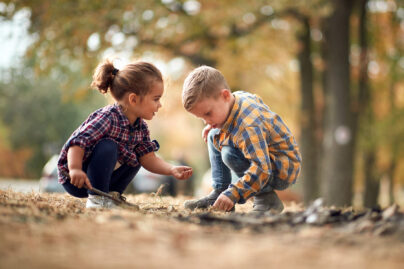 Tyttö ja poika leikkivät ruutupaidoissa syksyisessä maisemassa.