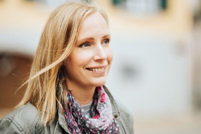 Vaaleahiuksinen nainen seisoo ulkona ja hymyilee