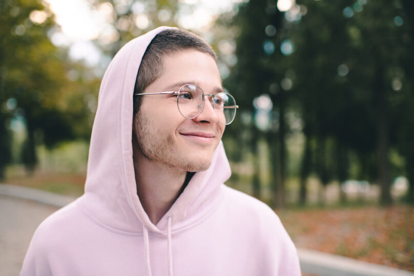 Nuori mies ulkona vaaleanpunainen huppari päällä ja huppu päässä