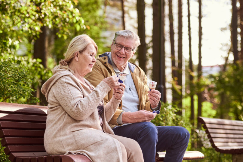 Omashoitaja ja omaishoidettava istumassa puiston penkillä syömässä jäätelöä