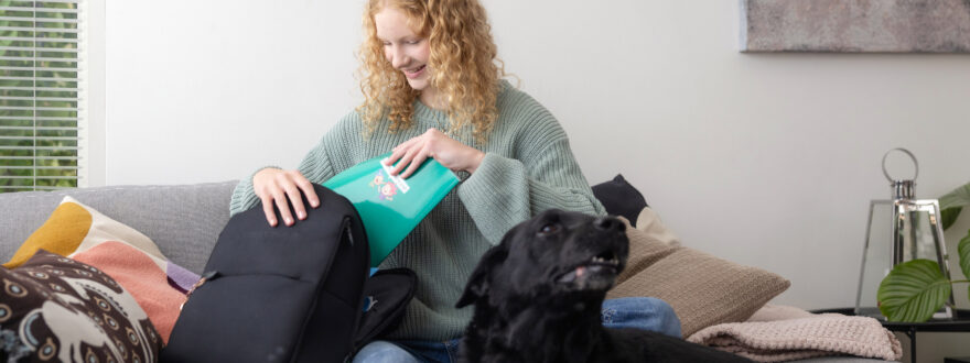 Teinityttö pakkaa reppua koiran ollessa vierellä.