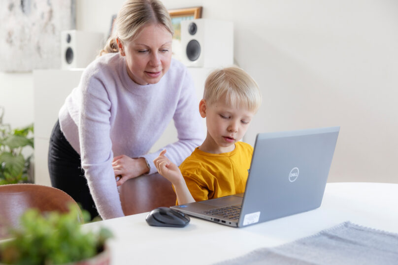 Coronaria kuntoutuspalvelujen lapsiasiakas on kotona äitinsä kanssa kannettavan tietokoneen äärellä.