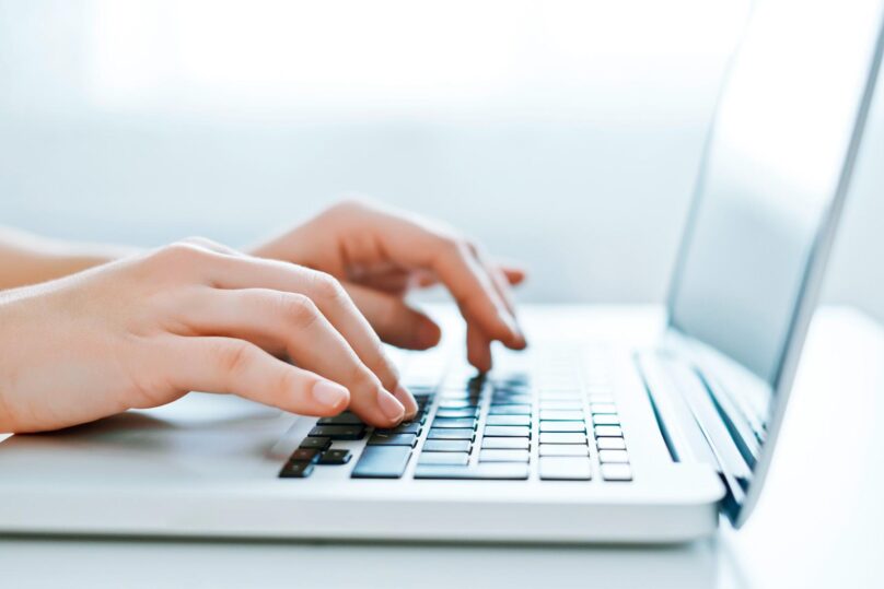 Lähikuva naisen käsistä käyttämässä kannettavaa tietokonetta.