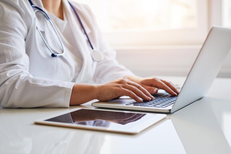 Lähikuva naislääkärin käsistä käyttämässä kannettavaa tietokonetta.