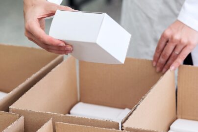 Lähikuvassa nainen pakkaamassa valkoisia paketteja ruskeisiin pahvilaatikoihin.