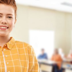 Punahiuksinen nuori nainen seisoo luokkahuoneen edessä näyttämässä sormilla ok-merkkiä.