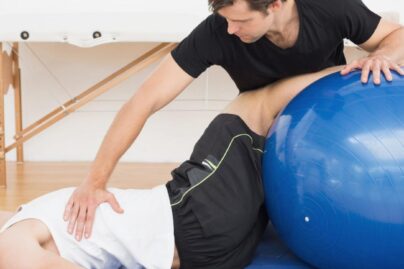 Fysioterapeutti auttaa nuorta miesasiakasta alaselkäkivussa jumppapallon avulla,