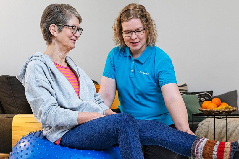 Coronarian ikääntyvien fysioterapian fysioterapeutti ohjaa asiakasta fysioterapialiikkeessä kotiympäristössä.
