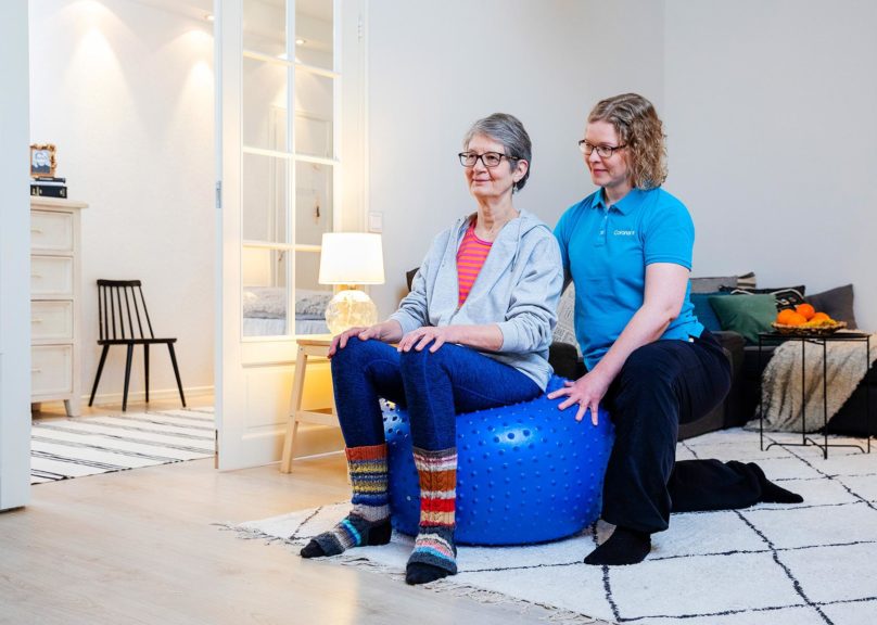Seniorifysioterapian naisasiakas ja fysioterapeutti kotiympäristössä.