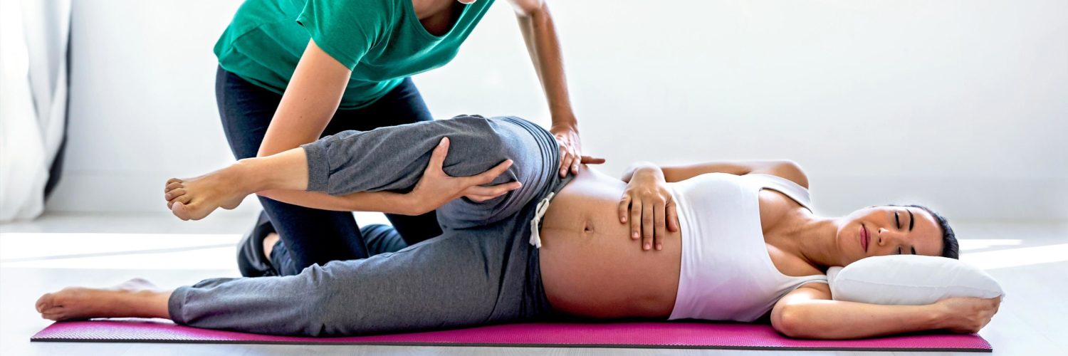 Raskaana oleva nainen makaa kyljellään jumppamaton päällä ja fysioterapeutti suorittaa venytystä alaraajaan.