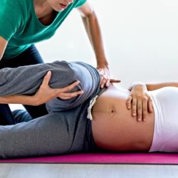 Raskaana oleva nainen makaa kyljellään jumppamaton päällä ja fysioterapeutti suorittaa venytystä alaraajaan.