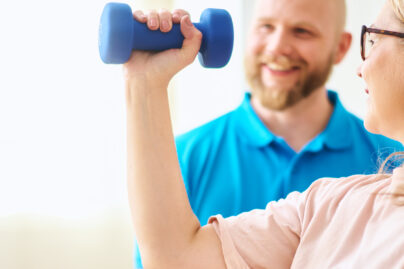 Naisasiakas tekee käsipainolla harjoitusta miesterapeutin ollessa taustalla tukena.