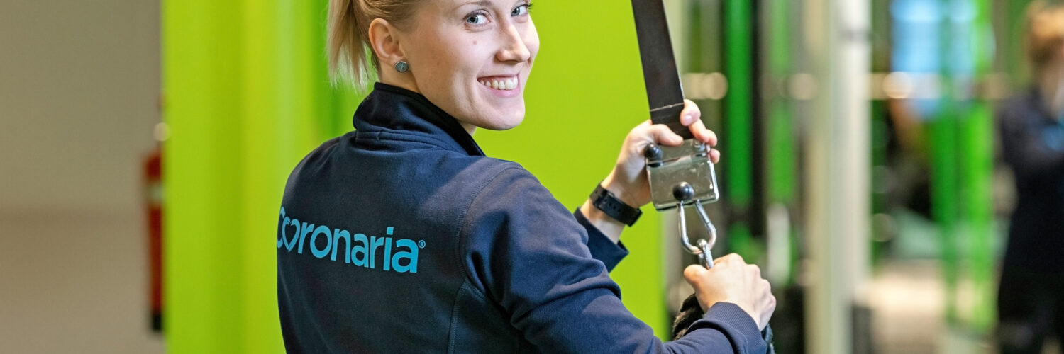 Coronarian naispuolinen terapeutti on kuntosalilla, katsoo olan yli ja hymyilee