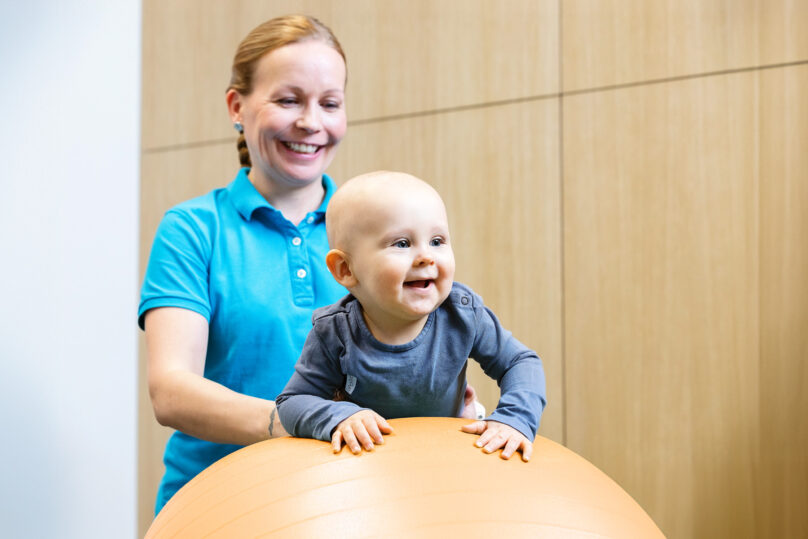 Vauva jumppapallon päällä naisterapeutin tukemana