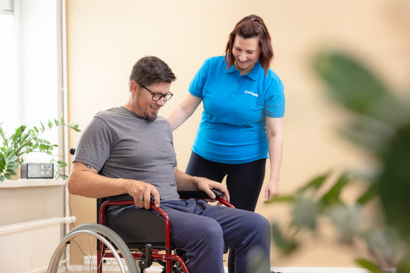 Miesasiakas istuu pyörätuolissa ja naisterapeutti on vieressä