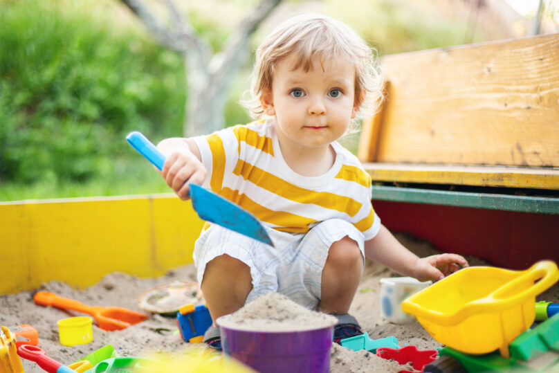 Pieni poika leikkimässä hiekkalaatikolla kesällä