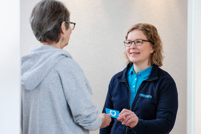 Naisterapeutti antaa Coronarian käyntikortin seniorinaiselle.
