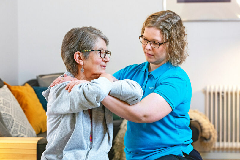 Iäkäs naisasiakas tekee kiertoliikettä ja naisterapeutti avustaa.