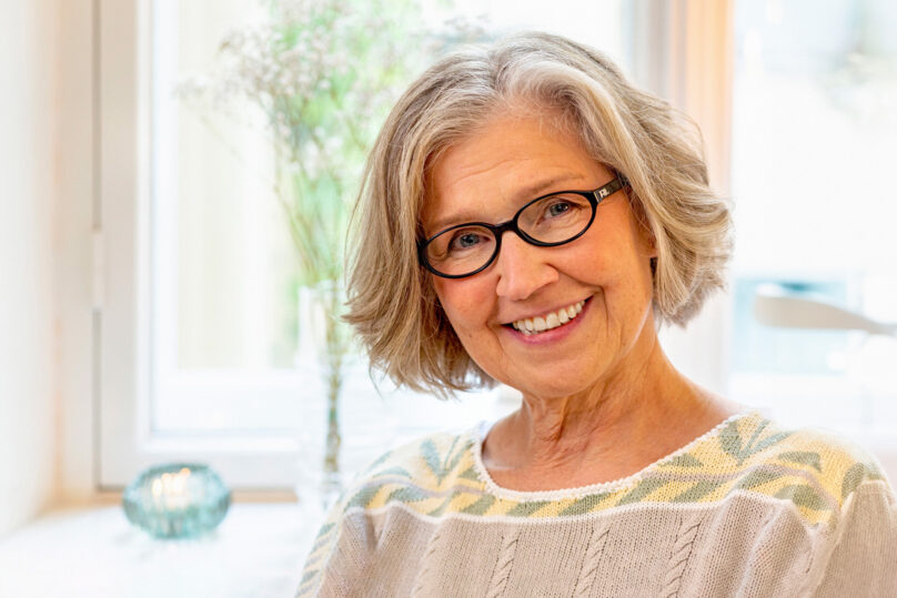 Vaaleahiuksinen seniorinainen hymyilee sisällä