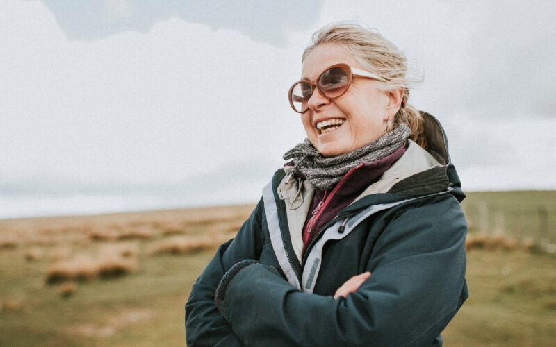 Keski-ikäinen nainen seisoo tuulisella rinteellä ja hymyilee.