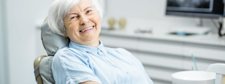seniori nainen hymyilee ja istuu hammaslaakarissa tuolissa