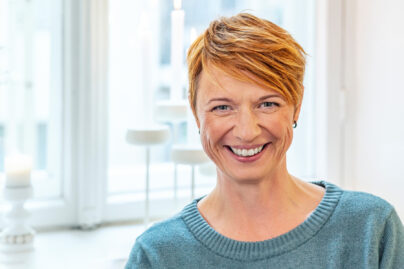 Punahiuksinen nainen katsoo kameraan ja hymyilee.