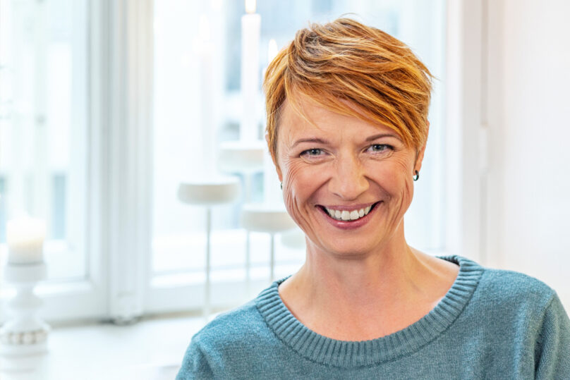 Punahiuksinen nainen katsoo kameraan ja hymyilee.