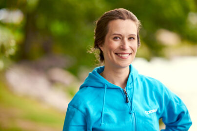 Tummahiuksinen nainen katsoo kameraan ja hymyilee.