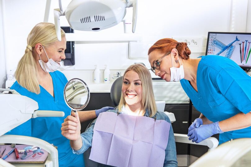 Potilas katsoo peilistä hampaiden valkaisun lopputulosta yhdessä hammaslääkärin ja hammashoitajan kanssa.