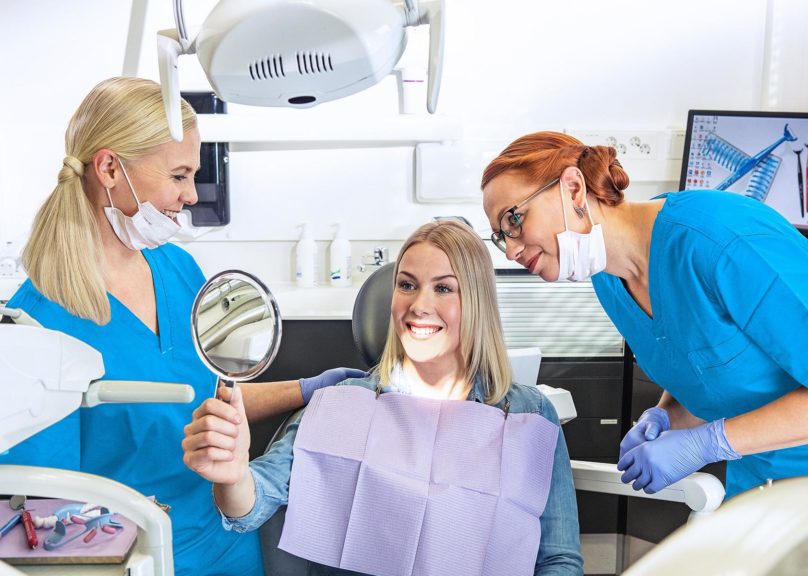 Potilas katsoo peilistä hampaiden valkaisun lopputulosta yhdessä hammaslääkärin ja hammashoitajan kanssa.