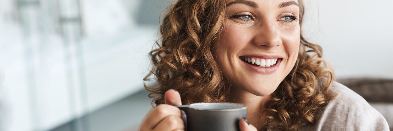 nainen hymyilee kahvikuppi kadessa