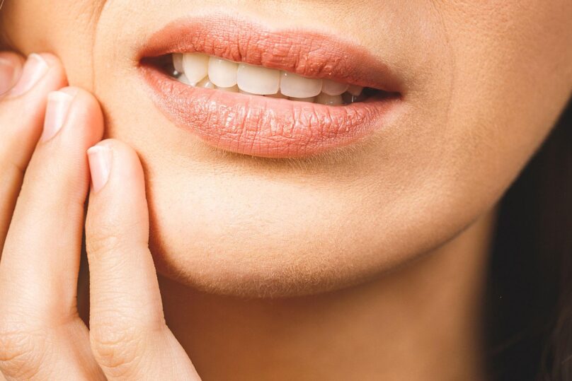 Nainen pitelee kiinni kipeästä hampaasta.