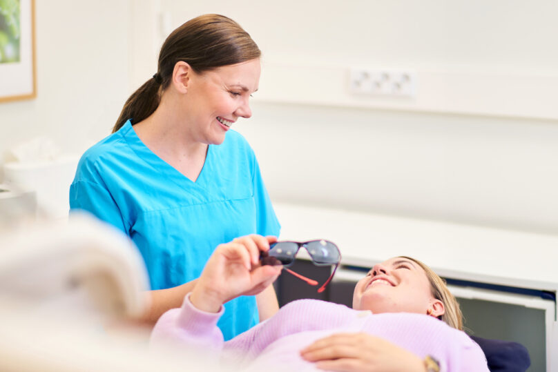 Hammaslääkäri katsoo potilasta ja ojentaa lasit.