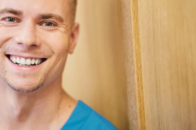 Sinipaitainen mies hymyilee tammiseinän edessä.