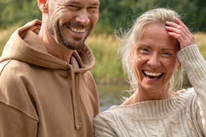 Nainen ja mies ovat ulkona vesistön äärellä ja hymyilevät kameraan.